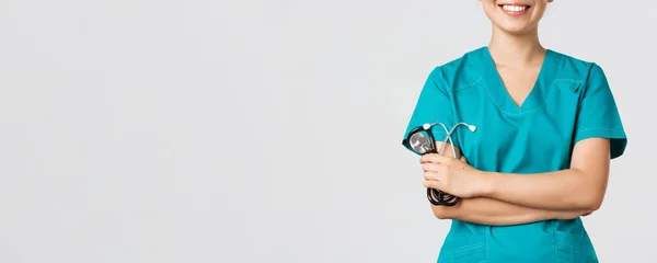 Covid-19, choroba koronawirusowa, koncepcja pracowników służby zdrowia. Przycięte zdjęcie azjatyckiej kobiety lekarz ciało uśmiechnięty, skrzyżuj ramiona klatki piersiowej pewnie i trzymając stetoskop, stojące białe tło — Zdjęcie stockowe