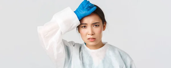 Ковід-19, коронавірусна хвороба, концепція медичних працівників. Молода втомлена азіатська жінка-лікар знімає особисте захисне обладнання і протирає поту, виглядаючи виснаженою після тривалої зміни в лікарні — стокове фото