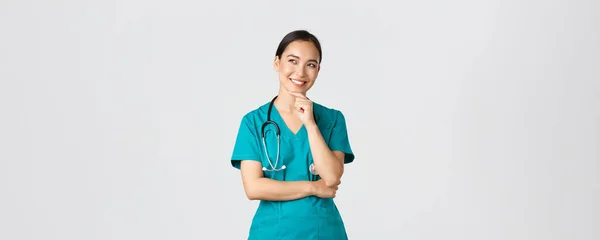 Covid-19, sjukvårdspersonal, pandemikoncept. Leende glad attraktiv asiatisk kvinnlig läkare i buskar, tittar övre vänstra hörnet och tänker, har idé, stående tankeväckande vit bakgrund — Stockfoto