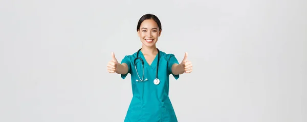 Covid-19, sjukvårdspersonal, pandemikoncept. Leende ganska asiatisk kvinnlig läkare, sjuksköterska i buskar se till att allt bra, visar tummen upp i godkännande, håller med eller som något, vit bakgrund — Stockfoto