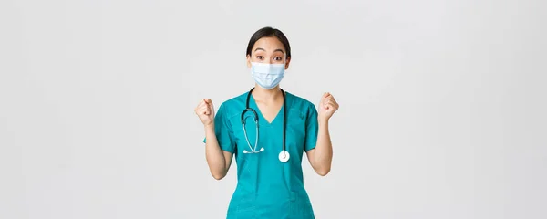 Covid-19, onemocnění koronavirem, koncept zdravotnických pracovníků. Vítězný veselý asijské žena lékař, lékař v lékařské masce a drhnutí, vypadat pozitivně, radovat se, řekněme hurá, bílé pozadí — Stock fotografie