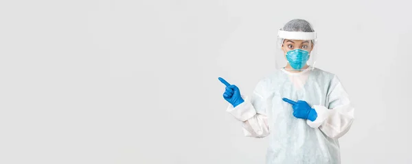 Covid-19, coronavirus disease, healthcare workers concept. Surprised female asian doctor, physician in medical respirator and personal protective equipment pointing upper left corner — Stock Photo, Image