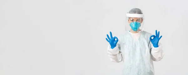 Covid-19, koronavírus betegség, egészségügyi dolgozók koncepciója. Magabiztos és komoly ázsiai női orvos, labortechnikus egyéni védőfelszerelésben, aki beleegyező gesztust mutat a jóváhagyásban — Stock Fotó
