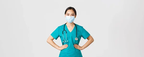 Covid-19, coronavirus ziekte, gezondheidswerkers concept. Zelfverzekerde professionele arts, arts in medisch masker en scrubs werken haar shift clinic, op zoek naar vastberaden, witte achtergrond — Stockfoto