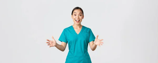 Ковид-19, медицинские работники, пандемия. Счастливая и удивленная азиатская медсестра в халатах поднимает руки взволнованно и улыбается. Доктор поздравляет с отличными новостями, аплодисментами, белым фоном — стоковое фото