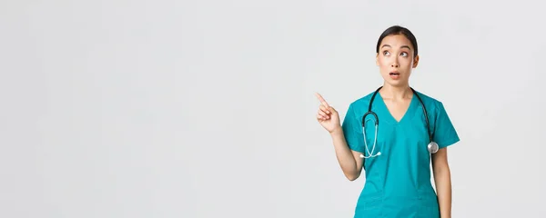 Covid-19，保健工作者，大流行病概念。惊讶而惊奇的亚裔女医生看着左上角,指指左上角.韩国医生神魂颠倒地盯着横幅做广告 — 图库照片