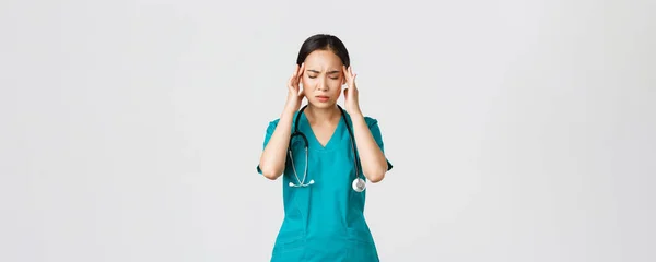 Ковід-19, медичні працівники, пандемія. Перевтомившись і втомившись, молода азіатська медсестра закриває очі, роздратуючись від головного болю, відчуває запаморочення, нічний зсув з пацієнтами з коронавірусом, білий фон — стокове фото