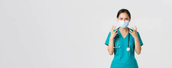 Covid-19, coronavirus disease, healthcare workers concept. Angry and pissed-off asian female doctor, physician in medical mask and scrubs, clench fists outraged, looking furious, white background — Stockfoto