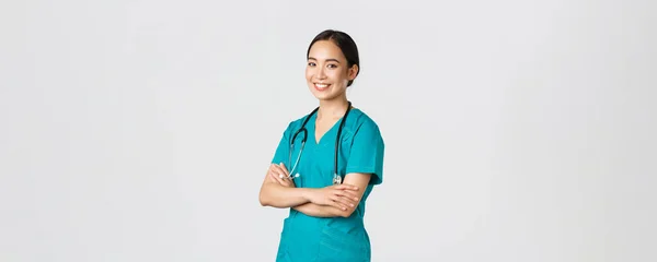 Covid-19, healthcare workers, pandemic concept. Professional confident, smiling asian female doctor, nurse in scrubs with stethoscope for examinations, cross arms and look at camera — Stock Photo, Image