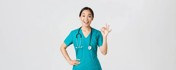 Covid-19, pracownicy służby zdrowia, koncepcja pandemii. Zaskoczony i szczęśliwy azjatycki lekarz, pielęgniarka w fartuchu wykazując się w porządku gest i uśmiech zdumiony, pochwała dobra robota, zgadzają się z kimś — Zdjęcie stockowe