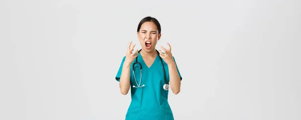 Covid-19, healthcare workers and preventing virus concept. Angry pissed-off asian female nurse, doctor losing temper, stressed-out physician shouting in anger, looking mad and aggressive — Stockfoto