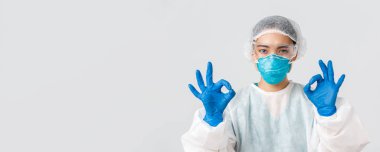 Covid-19, koronavirüs hastalığı, sağlık çalışanları konsepti. Kişisel koruma ekipmanlarıyla memnun olmuş, ciddi görünümlü Asyalı bir kadının yakın plan çekimi tamam bir jest yap, onayla ya da garanti et