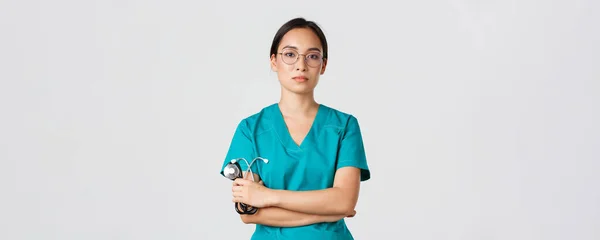 Covid-19, choroba koronawirusowa, koncepcja pracowników służby zdrowia. Profesjonalny pewny siebie, poważnie wyglądający lekarz, lekarz w okularach i fartuchach, trzymający stetoskop, stojące białe tło — Zdjęcie stockowe