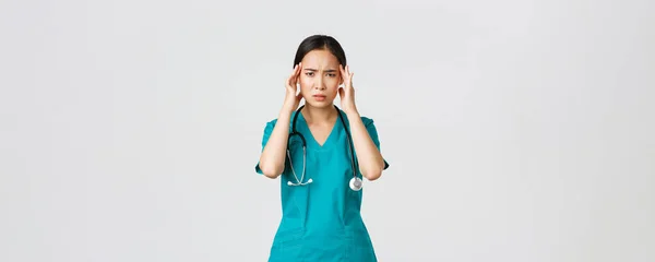 Covid-19, pracownicy służby zdrowia, koncepcja pandemii. Przepracowana i wyczerpana azjatycka lekarka, lekarz chory, noszenie fartuchów, dotykanie głowy, narzekanie na ból głowy lub wysoką gorączkę — Zdjęcie stockowe