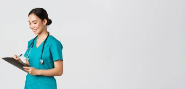 Sağlık çalışanları, virüsü önleme, karantina kampanyası konsepti. Güzel gülümseyen Asyalı doktor, hastaneye koşan hemşire hasta sonuçlarının yazılı olduğu panoya bakıyor, insanları muayene ediyor.