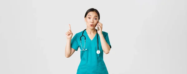 Covid-19, pracownicy służby zdrowia i zapobieganie koncepcji wirusa. Portret pięknej azjatyckiej lekarki, pielęgniarki w fartuchu rozmawiającej przez telefon i podnoszącej palec, jak masz świetny pomysł, pamiętaj, zasugeruj plan — Zdjęcie stockowe