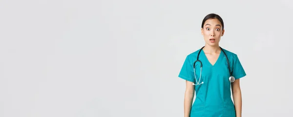 Covid-19, pracownicy służby zdrowia, koncepcja pandemii. Imponująca i zaskoczona azjatycka pielęgniarka w fartuchu opuszcza szczękę i gapi się na niemowę aparatu, wyglądając zdumiewająco na białym tle — Zdjęcie stockowe