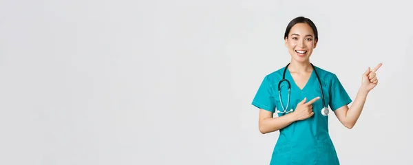 Covid-19, sağlık çalışanları, salgın konsepti. Gülümseyen Asyalı kadın doktor, önlüklü terapist sağ üst köşeyi işaret ediyor, check-up 'a davet ediyor, aşı öneriyor. — Stok fotoğraf