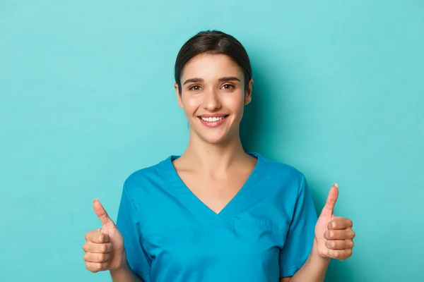 Coronavírus, distanciamento social e conceito de saúde. Close-up de enfermeira otimista em esfregaços, sorrindo e mostrando polegares para cima na aprovação, trabalhando com pacientes covid-19, fundo azul — Fotografia de Stock