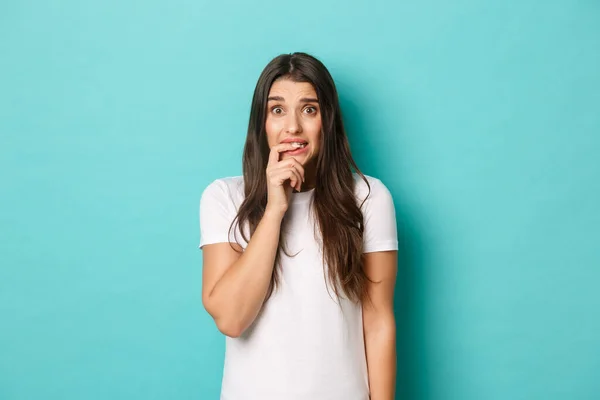 Image of insecure cute girl looking worried and indecisive, scared of something, biting finger and looking unsure, standing over blue background — Stock Photo, Image