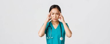 Sağlık çalışanları, virüsü önleme, karantina kampanyası konsepti. Aşırı çalışan ve yorgun Asyalı doktorların yakın plan fotoğrafları, baş ağrısı çeken, sorunlu görünen, ayakta duran beyaz arka plan