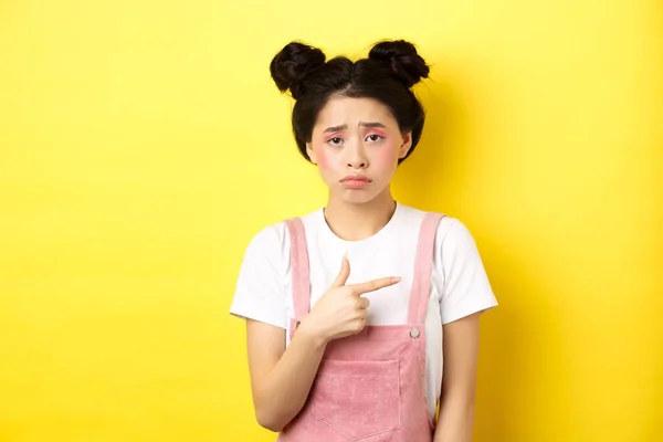 Smutná a zklamaná asijská dívka mračí, nefér, ukazuje prstem na špatnou věc, stěžuje si na něco znepokojivého, žluté pozadí — Stock fotografie