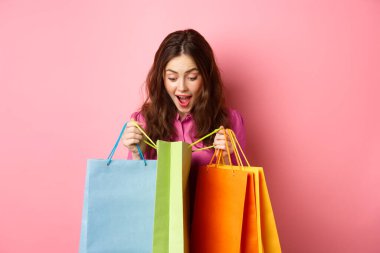 Heyecanlı kız alışveriş çantalarını açtı ve hayrete düştü. Mutlu yüzüyle hediyelere baktı. Pembe arka planda durdu.