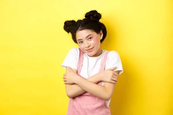 Sommerliches Lifestyle-Konzept. Nette asiatische Schönheit Mädchen mit Make-up, umarmt sich und lächelt romantisch, steht zart auf gelbem Hintergrund — Stockfoto
