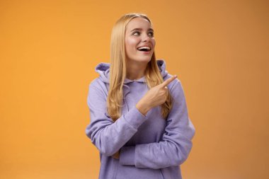 Neşeli, neşeli, kapüşonlu, neşeli Avrupalı kadın gülümseyen mutlu bir gülümseme ile dükkan alışverişinde ilginç bir performans sergiliyor, turuncu arka plan