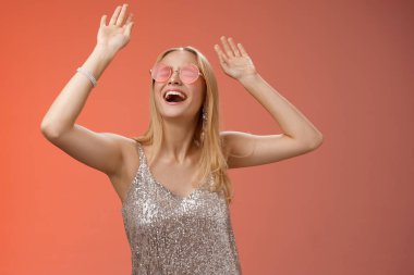 Heyecanlı, enerjik, genç, sarışın, gümüş renkli, şık gözlüklü, güneş gözlüklü, dans pistinde eğlenen, dans eden, gece kulübü partisi veren, doğum gününü kutlayan, kırmızı arka planlı genç bir kadın.