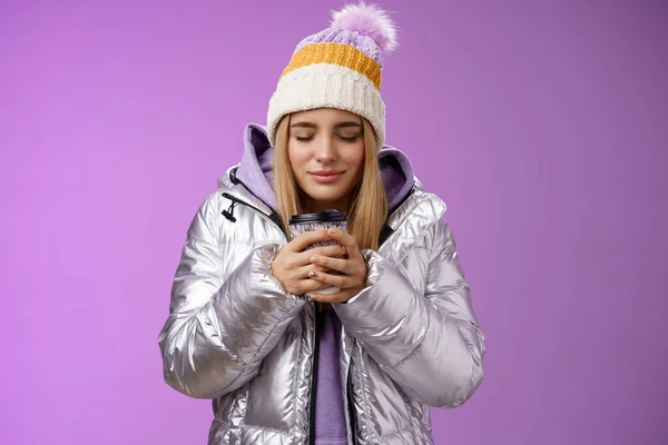 Charmante zarte romantische blonde Mädchen schnuppern schönen Geruch warm leckeren Kaffee halten Take-away-Tasse warme Hände schließen Augen freuen sich tragen Winterjacke Hut genießen Urlaub, lila Hintergrund — Stockfoto