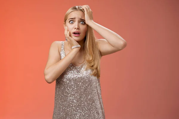 Sorprendido asustado inseguro pánico mujer rubio peinado en plata vestido tacto cabeza pop ojos asustado viendo aterrador crimen de pie estupor sin palabras jadeo sacudido, fondo rojo —  Fotos de Stock