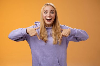 Heyecanlı, Avrupalı, sevimli, sarışın, güzel kız, gülümseyen, güler yüzlü, güler yüzlü, komik bakışlı, aşağıya bakan, harika, yeni bir ürün tavsiye eden, turuncu arka plan.