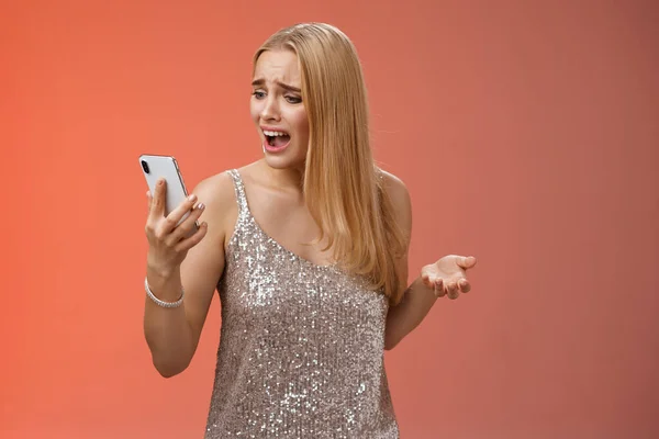 Беспокойная обеспокоенная высокомерная молодая блондинка жалуется кричать смартфон не может позвонить другу нет сигнала держа смартфон смотреть мобильный дисплей пьяный капризный спор, красный фон — стоковое фото