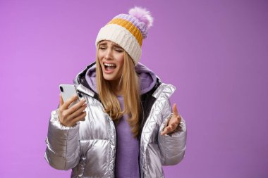 Rahatsız edici şikayetler, tatminsiz sarışın kız, aptal akıllı telefon diye bağırıyor, mutsuz bir şekilde mızmızlanıyor, cep telefonu sesi kaydediyor, üzgün, mor arka planda duruyor.