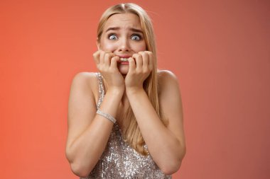 Korkmuş, genç, sarışın, paniklemiş, tırnak yiyen, patlak gözlü, korkmuş kamera dehşete düşmüş, nutku tutulmuşa benziyor.