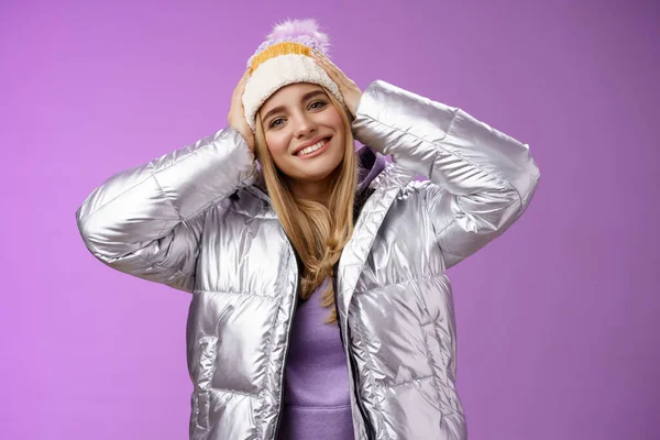 Zarte romantische attraktive blonde Frau genießen Winterurlaub Skigebiet Spaß Aussehen erfreut lächelnd breit geneigten Kopf berühren Hut trägt silberne Jacke, lila Hintergrund — Stockfoto