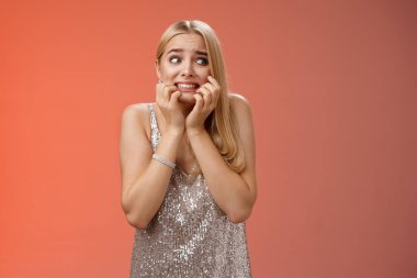 Korkmuş, kendine güveni olmayan, ürkek, genç, sarışın bir kadın korkudan titreyen, tırnak yiyen, patlayan gözler dehşete düşmüş kırmızı arka planda duran, dehşete düşmüş gümüş bir gece elbisesi giyiyor.