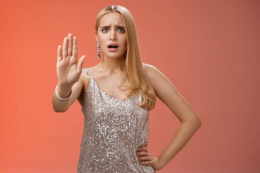 Freaked out displeased bothered insecure blond woman in silver glittering dress extend palm stop enough prohibition rejection gesture bothered pissed annoying clingy man nightclub, red background
