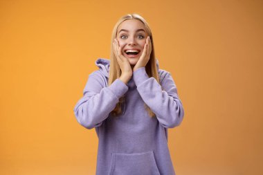 Şaşırtıcı derecede mutlu, şaşkın, sarışın kız arkadaş inanılmaz tatlı hediyeler alıyor. Çok tatlı, çok tatlı yanaklara dokunuyor, tatmin oluyor. Heyecanlı turuncu kapüşonlu arka planda dikiliyor.