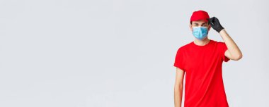 Covid-19, kendini karantina, online alışveriş ve nakliye konsepti. Dost canlısı teslimatçı adam müşteriyi yiyecek, paket teslimatı olarak karşılıyor. Kapı sapına kendi kendini karantinaya alıyor, tıbbi maske takıyor ve eldiven takıyor.