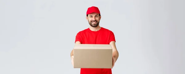 Consegna degli ordini, shopping online e concetto di spedizione del pacchetto. Cordiali sorridenti corriere barbuto in rosso uniforme t-shirt e cappuccio, dando fuori pacchetto per i clienti, consegna scatola al cliente — Foto Stock