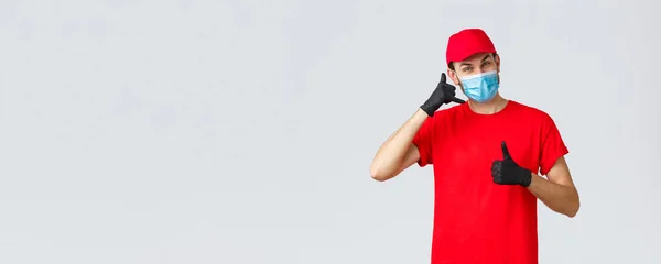 Covid-19, self-quarantine, online shopping and shipping concept. Friendly delivery guy in gloves and face mask, carrier uniform, show phone, asking call company order delivery, thumb-up — Stock Photo, Image