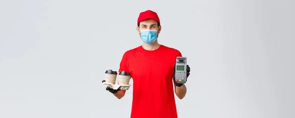 Takeaway, food and groceries delivery, covid-19 contactless orders concept. Friendly employee in red uniform, courier face mask and gloves, giving client POS terminal with coffee — Stock Photo, Image