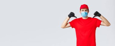 Erzak ve paket teslimatı, covid-19, karantina ve alışveriş konsepti. Kırmızı üniformalı, maskeli ve eldivenli kendine güvenen ciddi kurye teslimat hizmeti kalitesini arttırıyor.