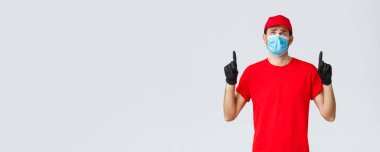 Covid-19, kendini karantina, online alışveriş ve nakliye konsepti. İsteksiz ve üzgün teslimatçı adam büyük bir paket taşımaz, iç çeker ve rahatsız olur. Kurye kötü haberi tepede görüyor.