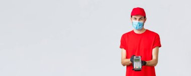 Bağlantı kurulamayan teslimat, ödeme ve kovid 19 sırasında online alışveriş, kendini karantina. Yüzü maskeli ve eldivenli hoş teslimatçı, kırmızı üniforma giyiyor, sipariş için ödeme yapan terminale ödeme yapıyor.