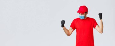 Covid-19, kendini karantina, online alışveriş ve nakliye konsepti. Cesaretli ve kendinden emin teslimatçı yumruk pompası, güçlü ve mutlu hisset, yumruk pompası evet diye bağır, amaca ulaş, yüz maskesi tak