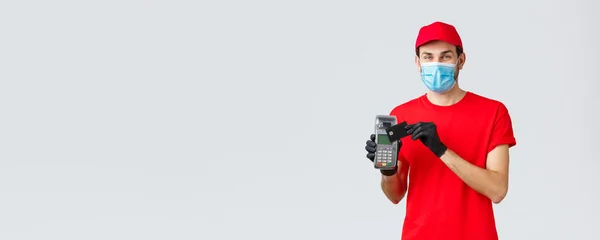 Contactless delivery, payment and online shopping during covid-19, self-quarantine. Friendly courier in red uniform, gloves and face mask, showing paying order with POS terminal and credit card — Stock Photo, Image