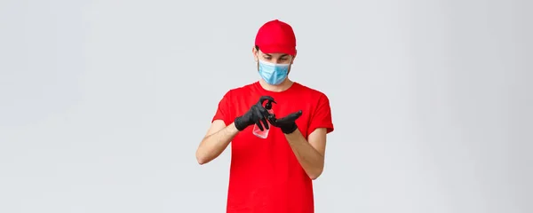Takeaway, παράδοση τροφίμων και ειδών παντοπωλείου, covid-19 έννοια ανέπαφων παραγγελιών. Courier ή υπάλληλος σε κόκκινο t-shirt και καπέλο ομοιόμορφη, φορούν μάσκα προσώπου και γάντια από καουτσούκ, εφαρμόστε απολυμαντικό χεριών — Φωτογραφία Αρχείου